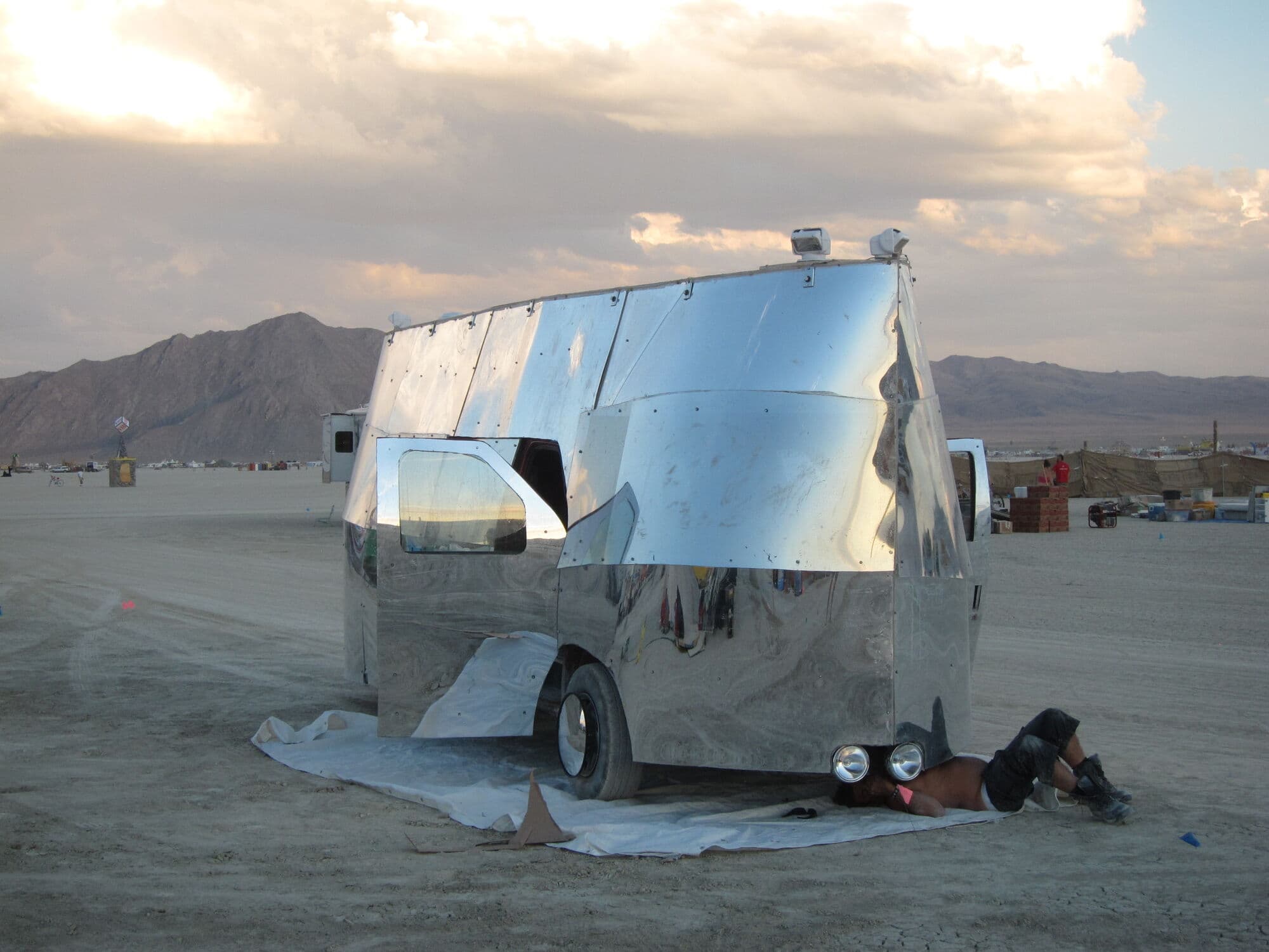 Mirage 1.0 — mirror-clad van on the playa at sunset, Brendan working underneath