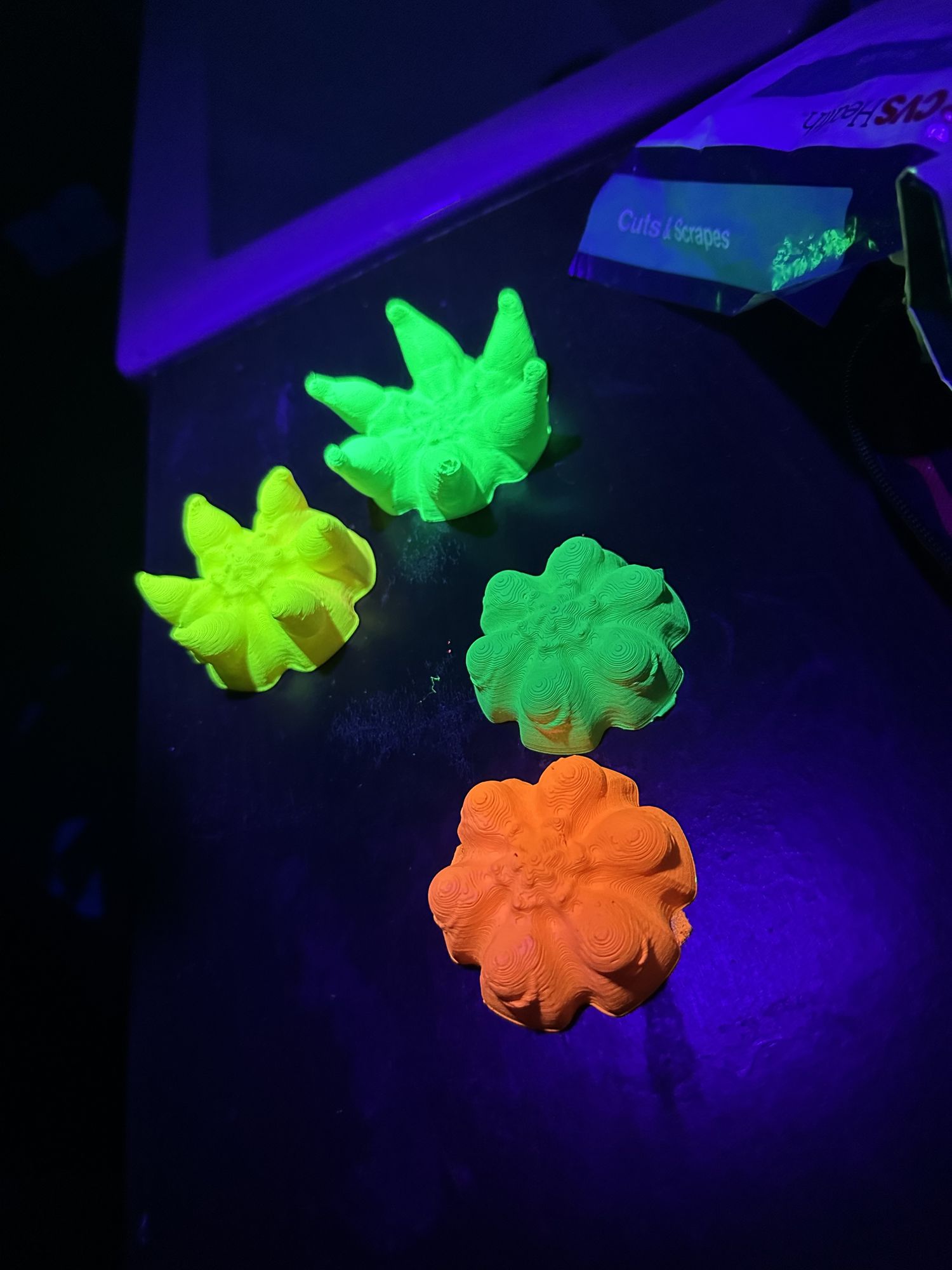 UV-reactive flower sculptures glowing under blacklight — green, yellow, orange